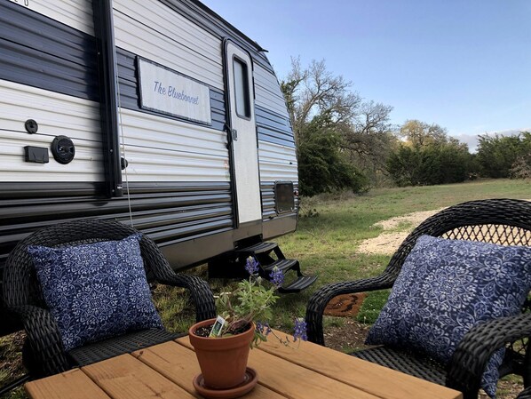 Une caravane baptisée « The Bluebonnet » était garée dans une zone herbeuse, où se trouvaient des chaises en osier et une table en bois.