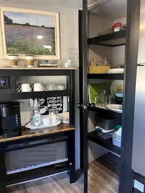 A kitchen with a coffee maker, cups, a sign, and a view of a field.