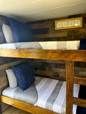 Un lit superposé avec une tête de lit en bois, une enseigne fixée au mur qui épelle le mot « DOZY », et un lambris en bois.
