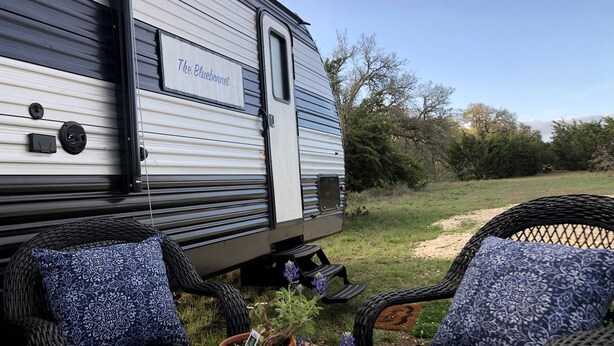 A caravan named 'The Bluebonnet' parked in a grassy area with wicker chairs and a wooden table.