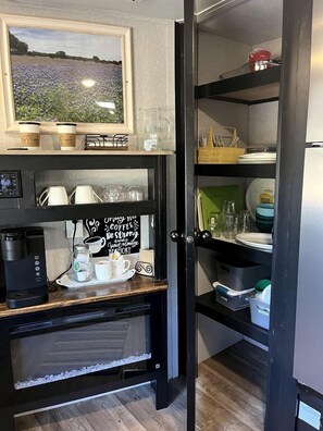 Una cocina con cafetera, tazas, un cartel y vistas a un campo.