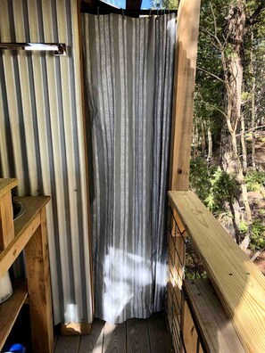 Une terrasse en bois avec une rambarde en métal, un banc en bois et un rideau.