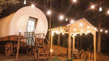 A covered wagon with a canopy, wooden steps, and a small wooden structure with lights.