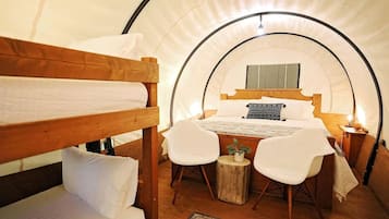 Ein gemütlicher, kreisrunder Raum im Zeltstil mit einem Etagenbett, einem Einzelbett, einem kleinen Tisch mit Stühlen und einer Nachttischlampe.