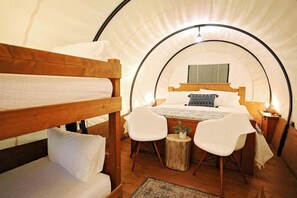 Ein gemütlicher, kreisrunder Raum im Zeltstil mit einem Etagenbett, einem Einzelbett, einem kleinen Tisch mit Stühlen und einer Nachttischlampe.