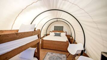 A tented room with a bunk bed, a single bed, a desk, and a chair.