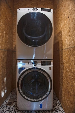Una lavadora y secadora apiladas en una habitación con paredes de madera y piso estampado.