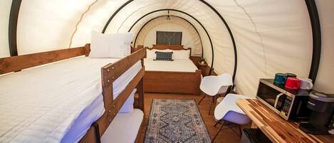 A tent-style room with bunk beds, a desk, a chair, a microwave, and a coffee maker.