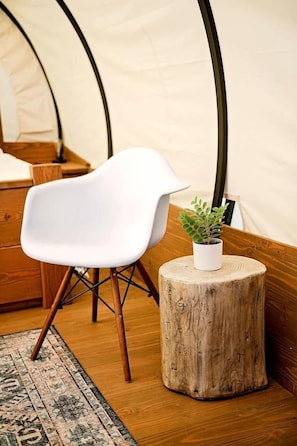 Una carpa con una silla blanca, un taburete de madera con una planta y una alfombra estampada.