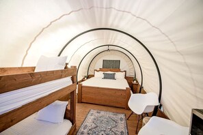 Ein Zeltraum mit einem Etagenbett, einem Einzelbett, einem Schreibtisch und einem Stuhl.
