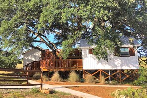 A white house with a wooden deck, surrounded by trees. - Delightful Dripping Springs Rental for a Tranquil Getaway in Texas (Dripping Springs)