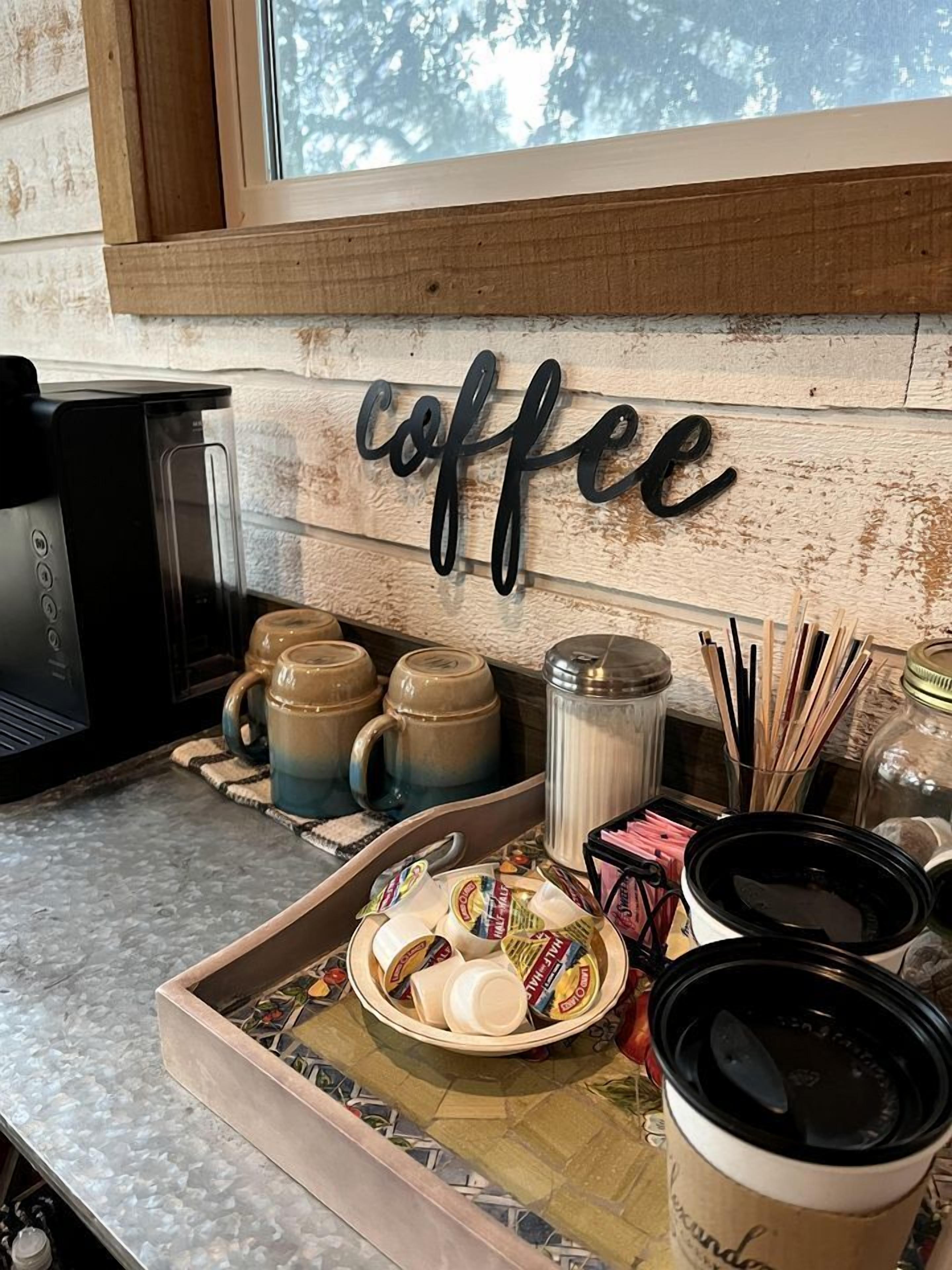 A kitchen area with a coffee station, including mugs, a coffee maker, and a tray with condiments.