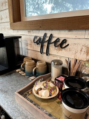 A kitchen area with a coffee station, including mugs, a coffee maker, and a tray with condiments.