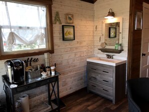 A rustic kitchen with wooden walls, a coffee station, a sink, and a mirror. - Delightful Dripping Springs Rental for a Tranquil Getaway in Texas (Dripping Springs)