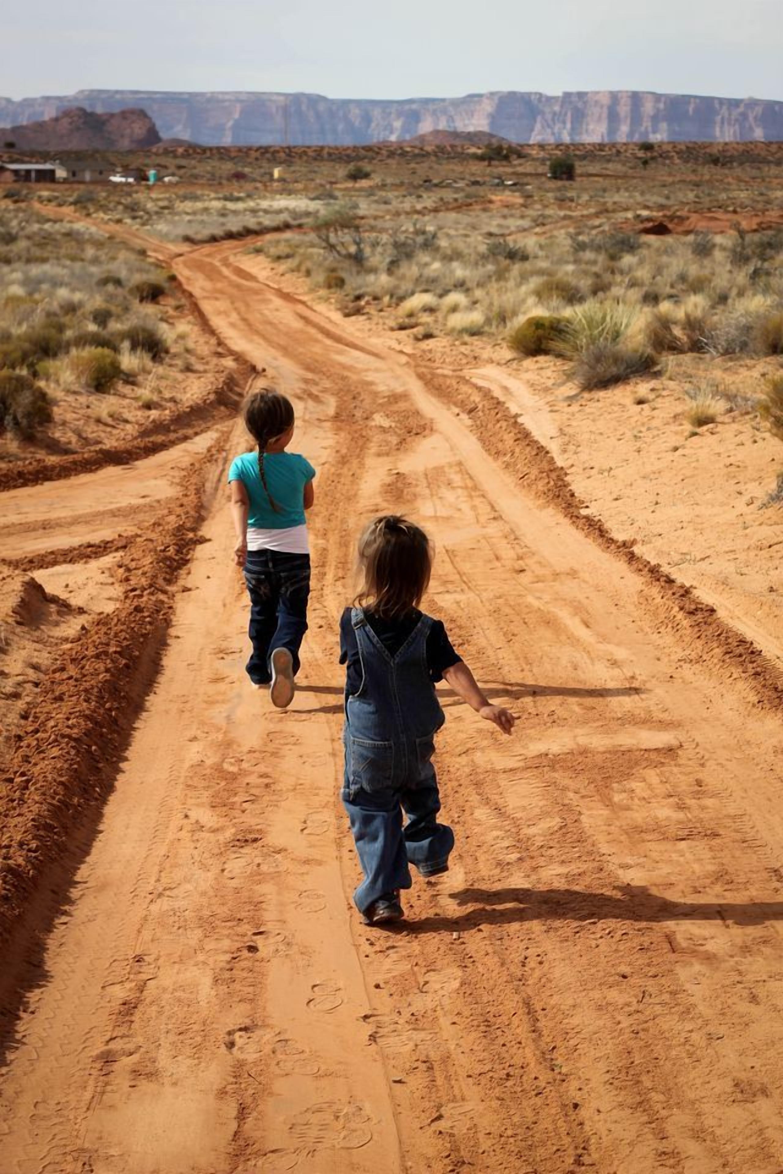 Two children walking on a dirt road in a desert landscape.