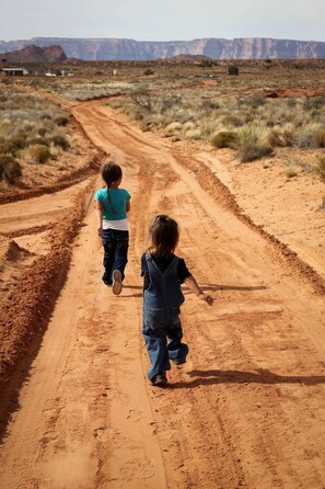 Deux enfants marchent sur un chemin de terre dans un paysage désertique.