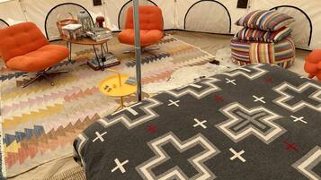 A tented room with orange chairs, a small table with books, a patterned rug, and a bed with a geometric blanket.