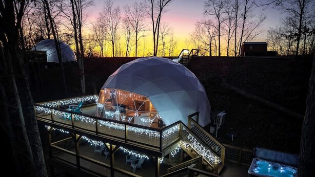 Una estructura de domo geodésico con un patio cubierto, mobiliario exterior y un jacuzzi.