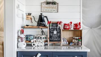 A kitchen with a coffee maker, mugs, a chalkboard sign, and a shelf with jars.