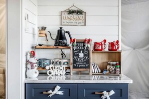 Une cuisine équipée d’une machine à café, de tasses, d’un tableau noir et d’une étagère remplie de bocaux.