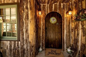 A rustic wooden door with a stained glass window, a green-framed window, and a welcome mat.