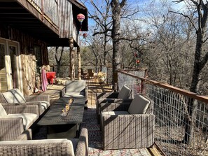 An outdoor patio with wicker furniture, a dining table, and a red tablecloth. - Magical Treehouse with Slide by Brazos River for Family Glamping Adventures in Texas (Weatherford)
