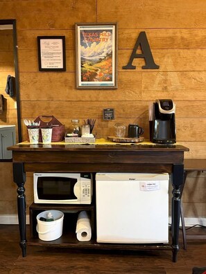Eine Küchenzeile mit Kaffeemaschine, Mikrowelle und Kühlschrank, sowie eine Holzwand mit einem gerahmten Poster und einem großen Buchstaben 'A'.