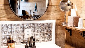 A bathroom with a wooden wall, a round mirror, a sink with a faucet, and a bottle of hand soap.
