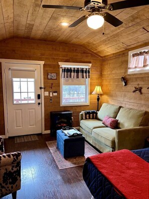 A cozy room with a ceiling fan, a window with a plaid valance, a couch, a lamp, and a fireplace.