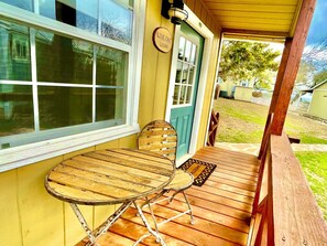 A wooden deck with a table and chairs, a door with a sign, and a window. - Gorgeous Texas Hill Country Rental near Austin for a Relaxing Getaway in Texas (Dripping Springs)