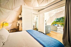 A tented room with a bed, a small table, and a view of an outdoor seating area.