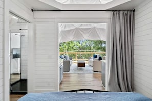 Una habitación con cama, vista a un área de estar al aire libre y ventana con cortinas.