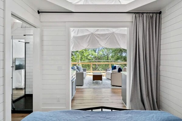 Una habitación con cama, vista a un área de estar al aire libre y ventana con cortinas.
