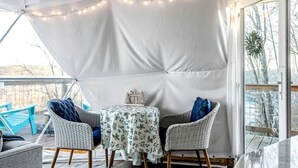 Un espacio al aire libre techado con una mesa, sillas, luces colgantes y vistas al exterior.