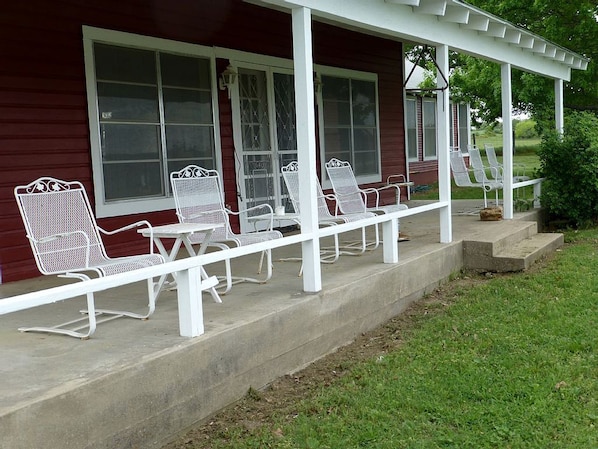 A covered porch with white metal chairs and a concrete floor.