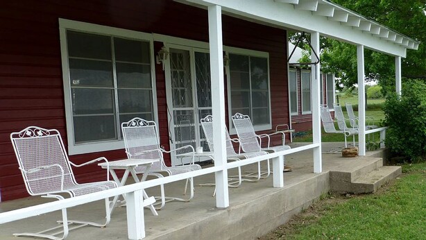 A covered porch with white metal chairs and a concrete floor. - Spacious Cottage Rental for Group Getaway on Ranch near Dallas, Texas (Weatherford)