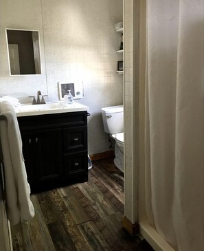 A bathroom with a white sink, black cabinet, white toilet, and wooden flooring. - Spacious Cottage Rental for Group Getaway on Ranch near Dallas, Texas (Weatherford)