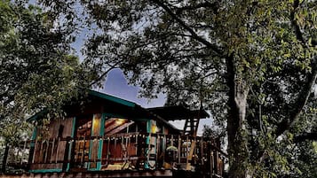 A wooden treehouse with a balcony, surrounded by dense foliage.