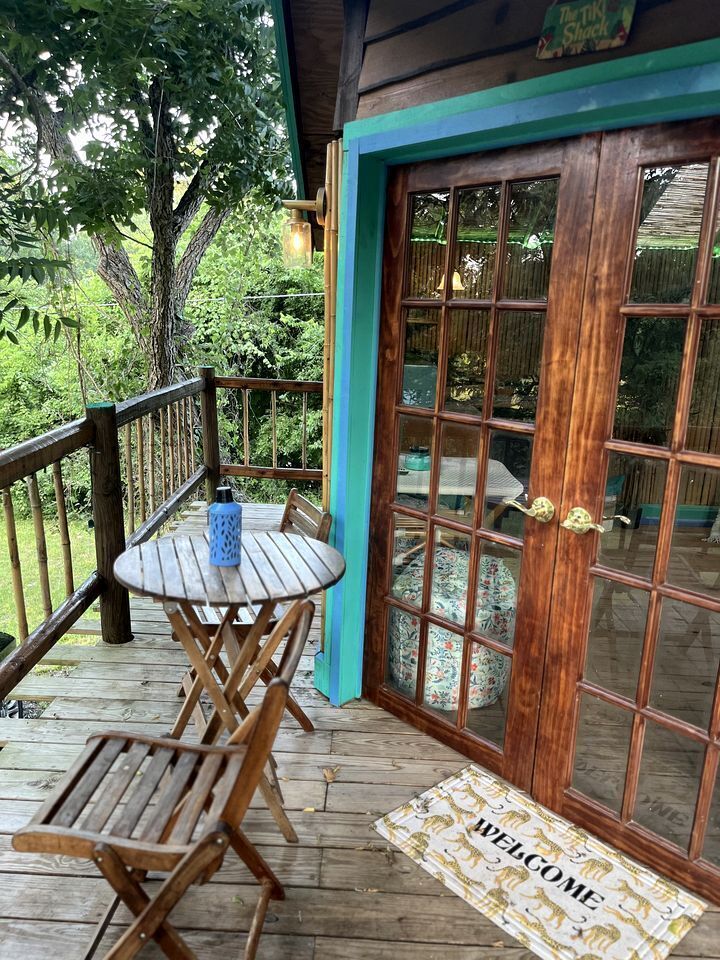 A wooden deck with a table and chairs, a glass door with a welcome mat, and a sign above the door.