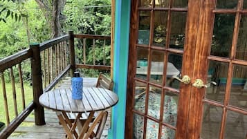 A wooden deck with a table and chairs, a glass door with a welcome mat, and a sign above the door.
