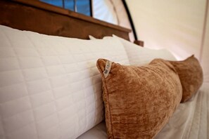 A bed with a quilted white mattress and a brown pillow.