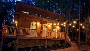 A wooden cabin with a balcony, stone foundation, and string lights.