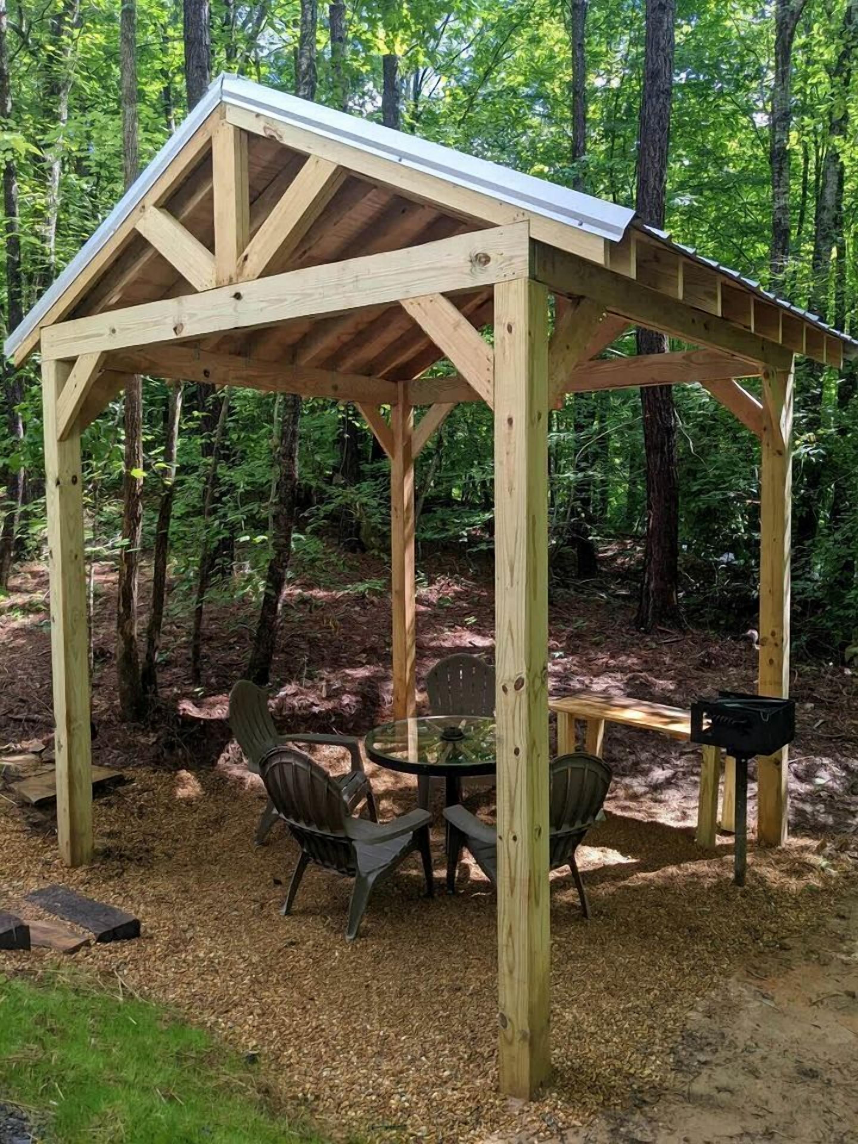 Un belvédère en bois, avec une table et des chaises, entouré d’une forêt.