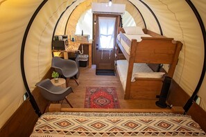 Un intérieur chaleureux dans une tente en forme de dôme, avec un lit superposé, un petit bureau, une chaise et un tapis.