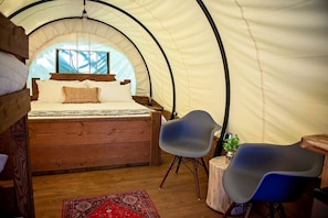 A tented room with a bed, two chairs, a small table, and a red rug.