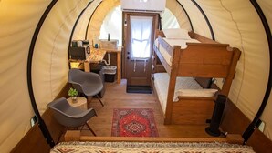 A cozy interior of a dome-shaped tent with a bunk bed, a small desk with a chair, a table with a plant, and a patterned rug.
