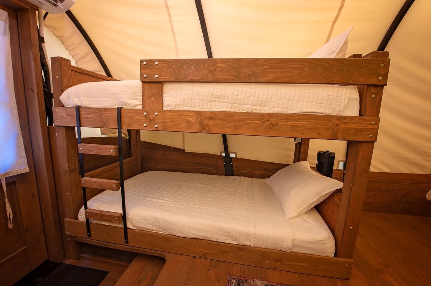A bunk bed with a wooden frame and white bedding inside a tent-like structure.