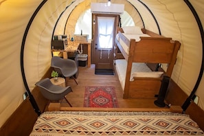 A cozy interior of a dome-shaped tent with a bunk bed, a small desk with a chair, a table with a plant, and a patterned rug. - Wonderful Wagon Rental with Fire Pit Surrounded by Nature in Tennessee (Benton)