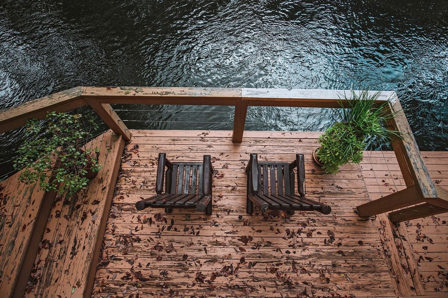 A wooden deck with two wooden benches and potted plants.