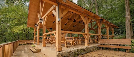 Un pavillon en bois, doté de fondations en pierre, entouré d’une terrasse en bois et de bancs.